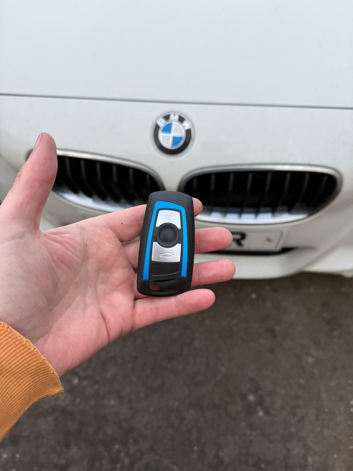 Hand holding a blue and black BMW car key fob with a vehicle in the background