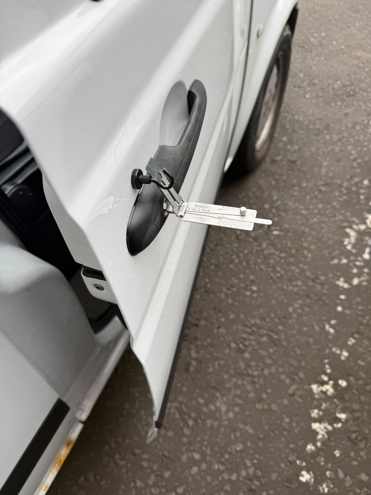 White car door handle with a lock pick tool being used for non-destructive vehicle entry